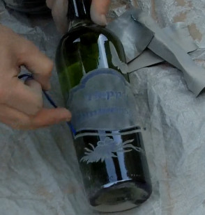 Finishing the sandblasted wine bottle by removing the stencil.